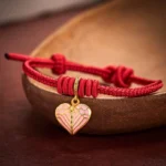 Red string braided heart charm bracelet with adjustable knot displayed on dark wooden bowl
