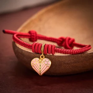 Red string braided heart charm bracelet with adjustable knot displayed on dark wooden bowl