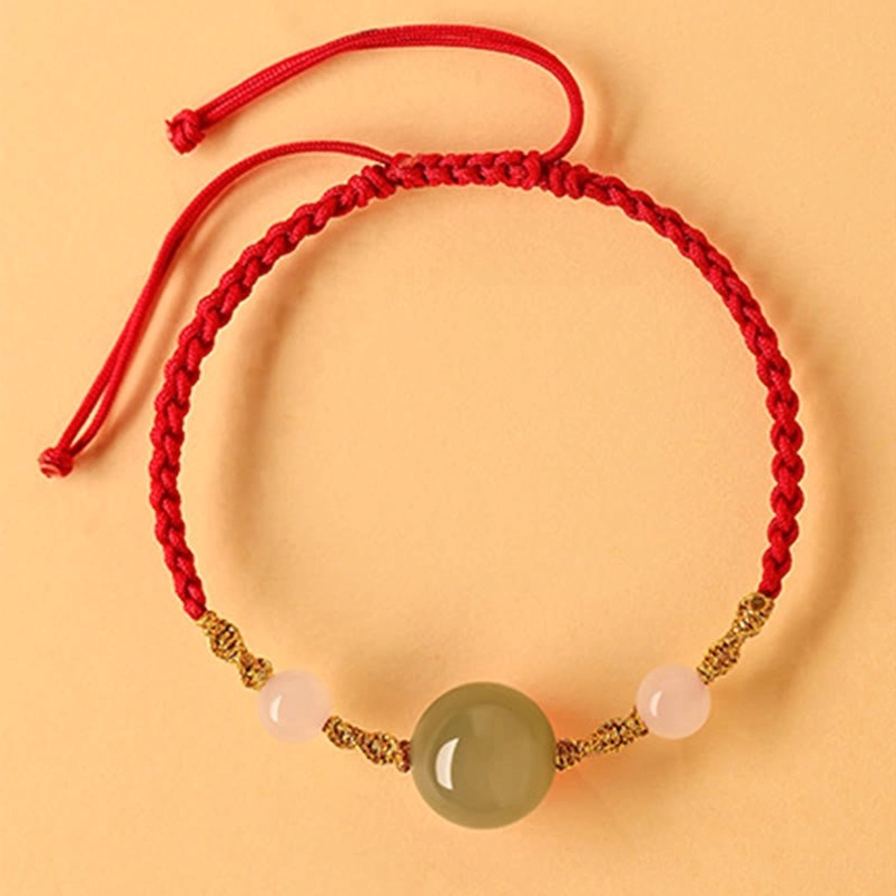 Red rope Hetian jade bracelet with white beads and gold accents, flat lay on orange background