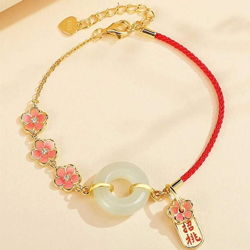 Red rope hetian jade bracelet with gold metal, enamel flower charms and peace buckle on beige background
