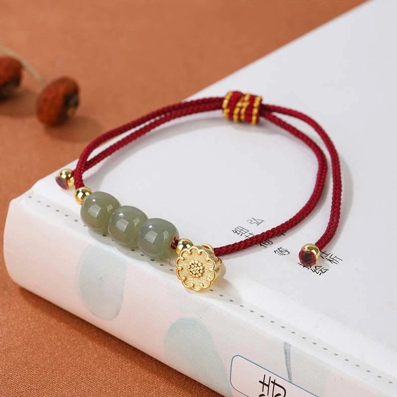 Red braided string Hetian jade lotus pod bracelet placed on vintage Chinese poetry book