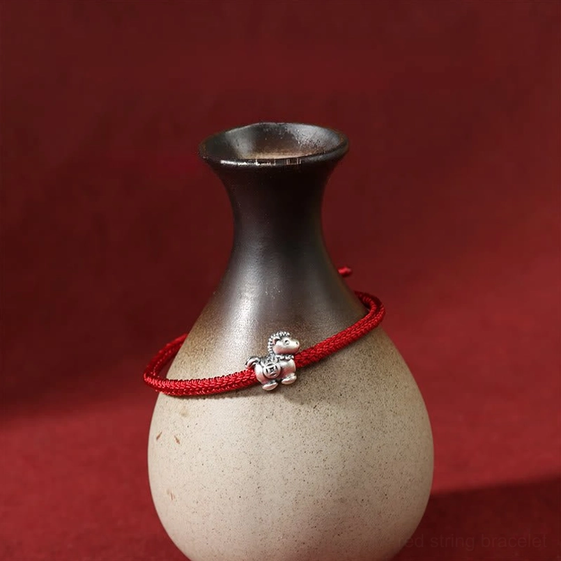 Handmade red cord silver horse zodiac bracelet draped on ceramic vase product detail