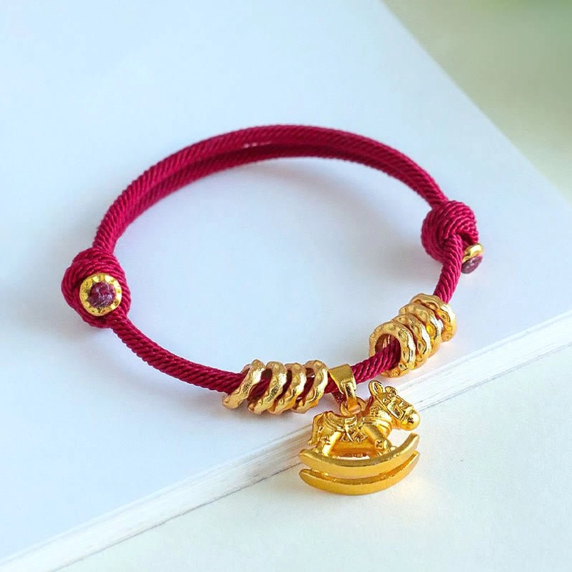 Red string horse bracelet with purple gemstone accents on light blue gradient background