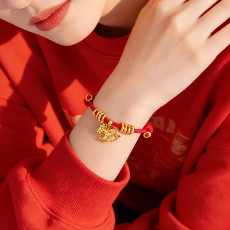 Close up view of worn red string horse charm bracelet on wrist with red sweater