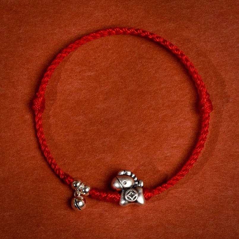 Red string bracelet with Year of the Horse silver charm and bell pendant overhead flat lay view