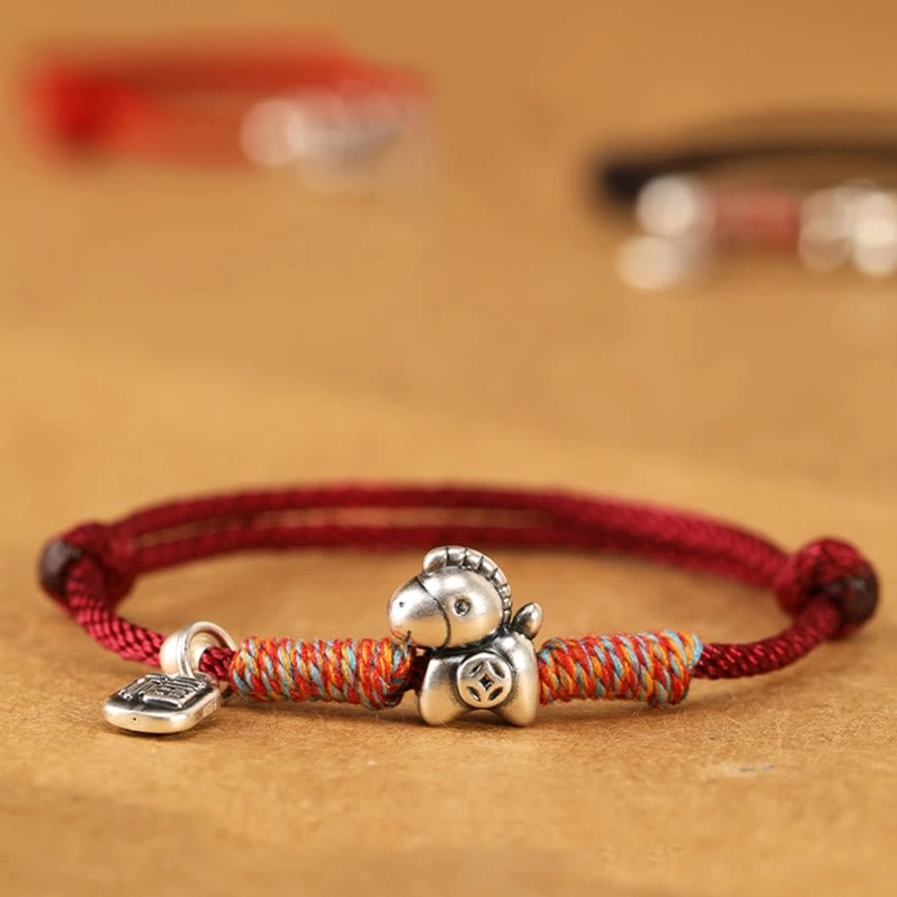 Red cord horse fu charm bracelet with dual adjustable knots angled flat lay view