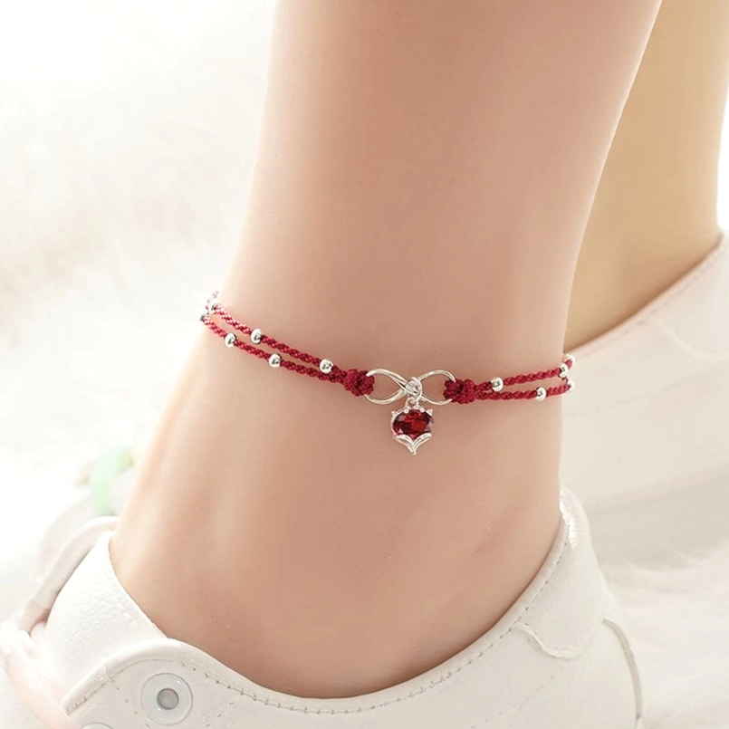 Double-layered red string anklet with infinity charm and heart drop on ankle, paired with white sneakers