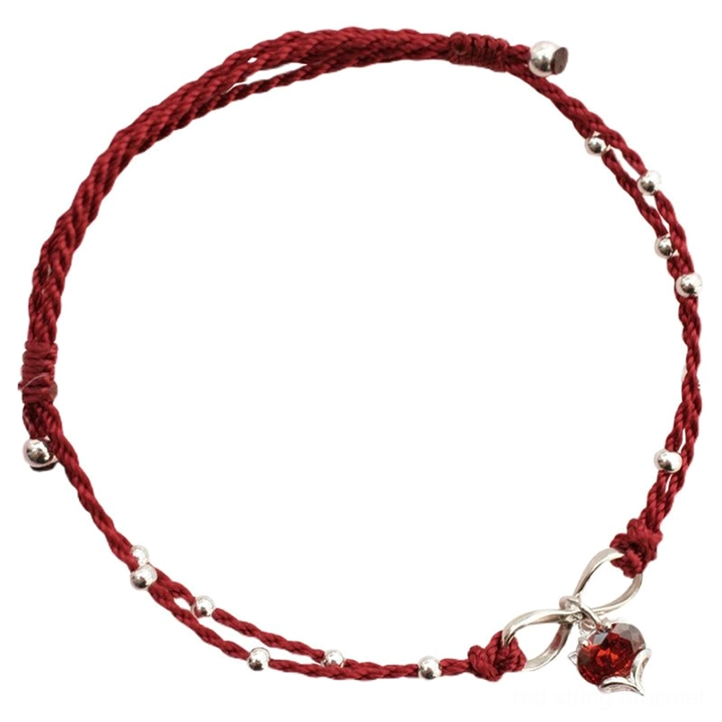 Top-down flat lay of double-layered red string ankle bracelet with infinity clasp and heart pendant