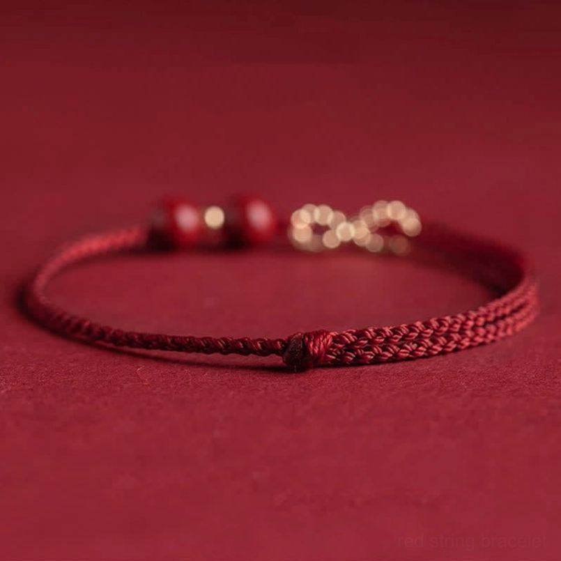 Red string jewelry with gold infinity symbol and cinnabar beads, side angle flat lay view