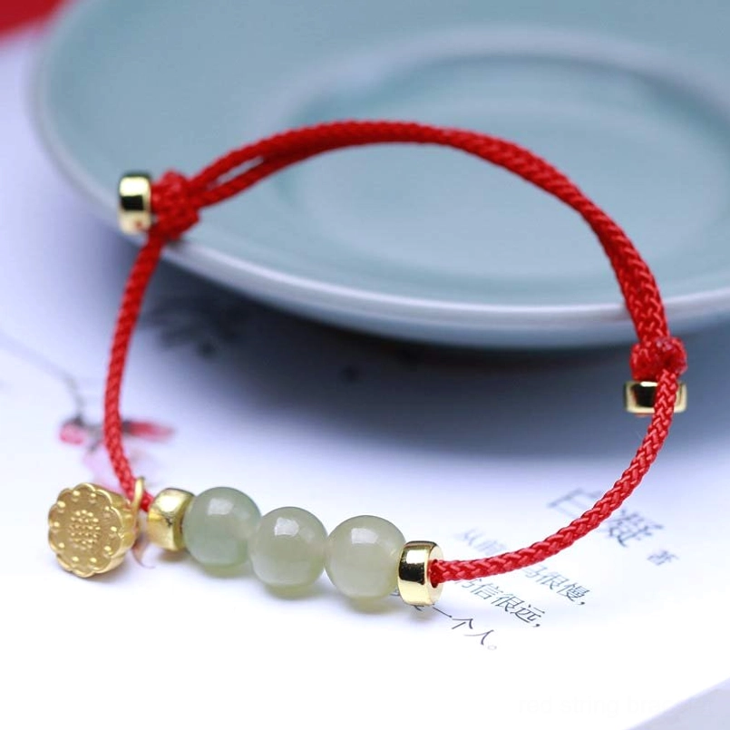 Red woven string jade bracelet with gold medallion charm detail on ceramic plate