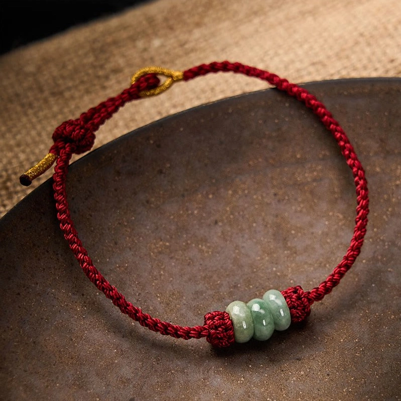 Red string jade protection bracelet on dark ceramic plate minimalist style