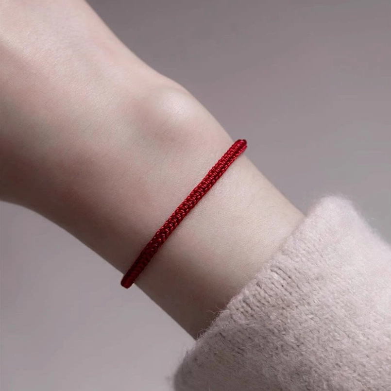 Close up of red string jade bracelet worn on wrist with casual knit sleeve