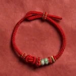 Red string jade bracelet with golden knots on red fabric background