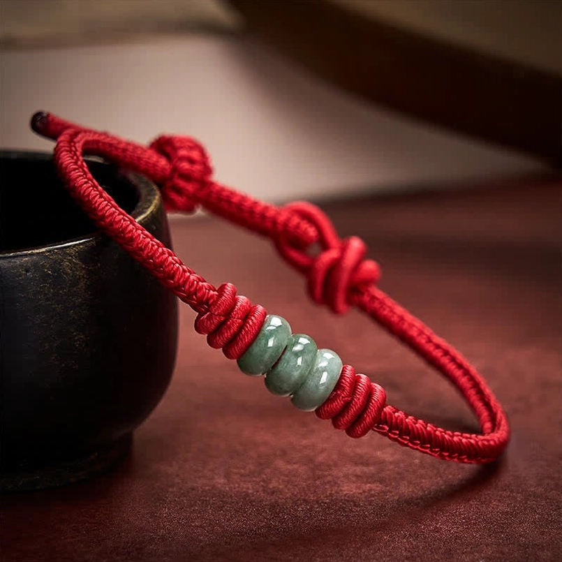 Adjustable red string jade bracelet with sliding knot displayed on dark ceramic tableware