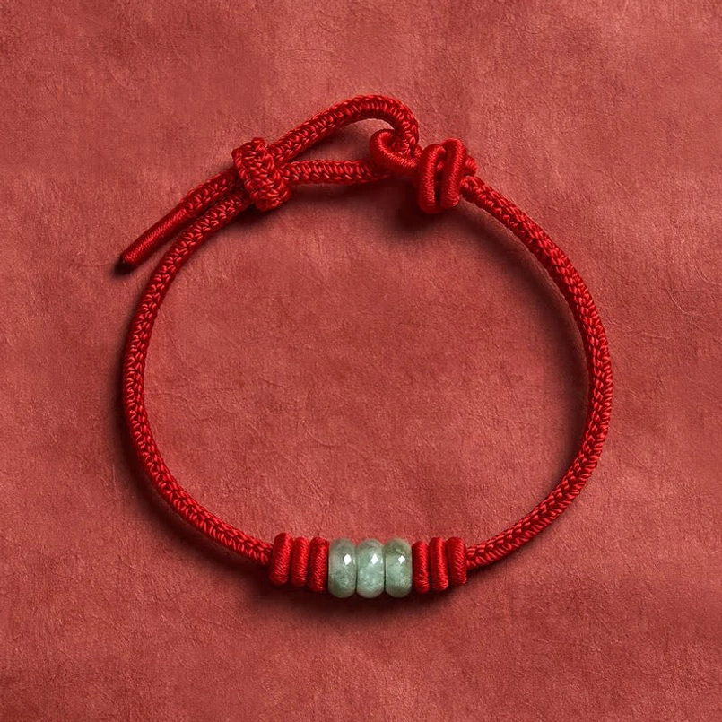 Red string jade bracelet with toggle knot adjustment system shown in flat lay composition