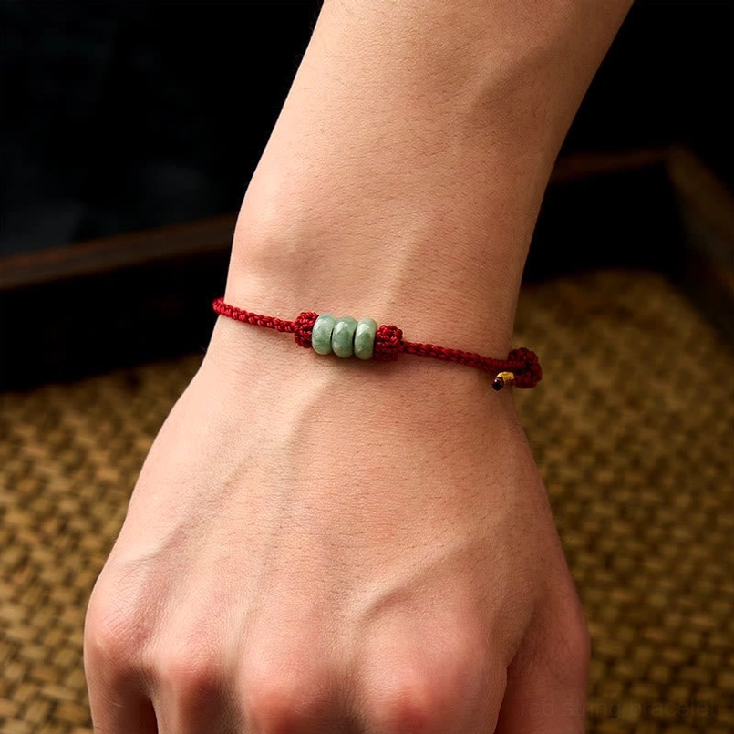 Adjustable red string jade bracelet worn on human wrist close-up view