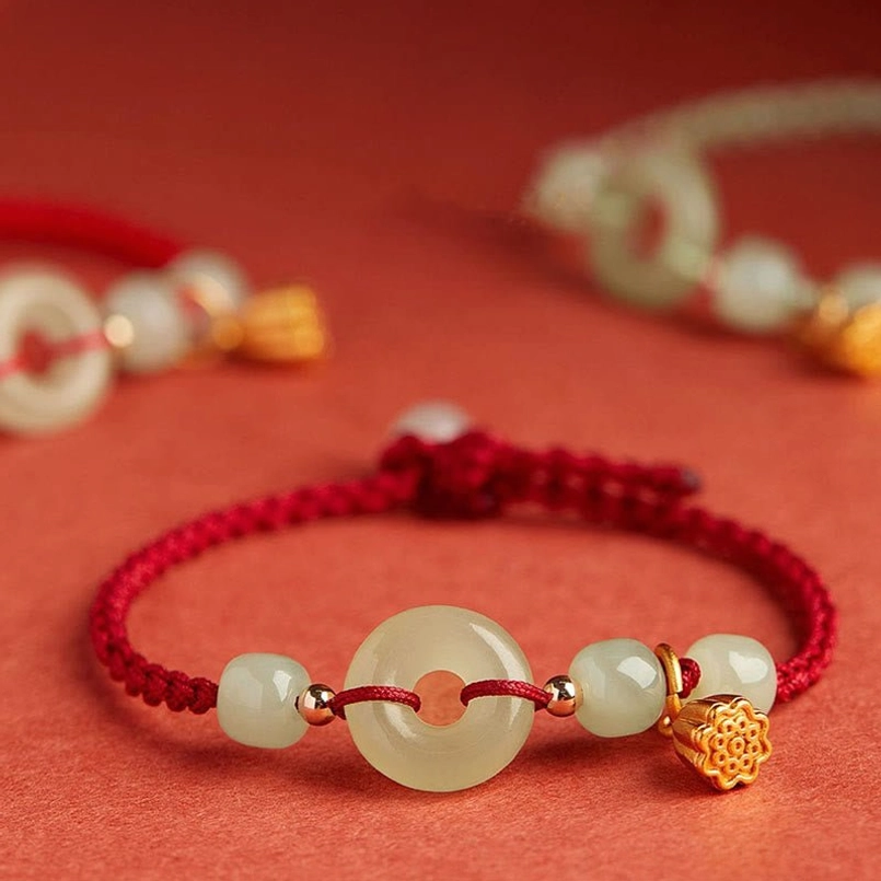Multiple red string jade bracelets with lotus charms overhead view
