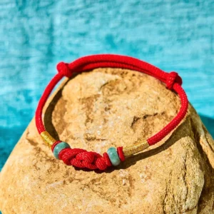 Red string jade couple bracelet with braided knot and gold accents displayed on stone