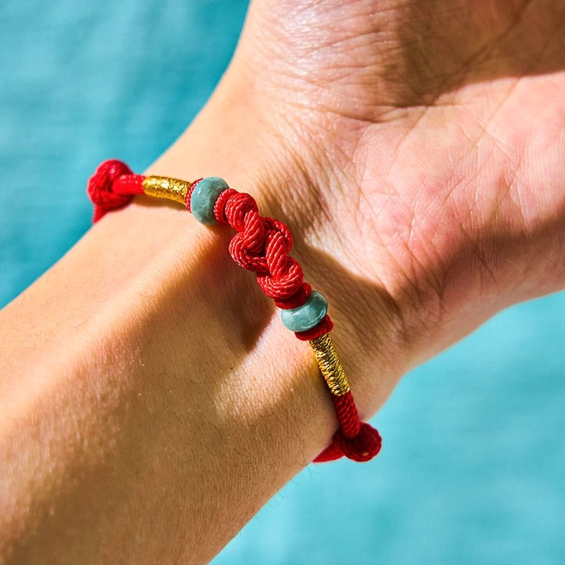 Matching red string jade bracelet on wrist showing secure fit and gold accents