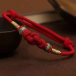 Red string jade fortune knot bracelet with gold accents - top view close-up