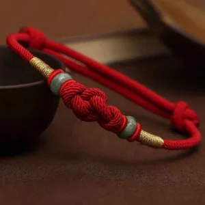 Red string jade fortune knot bracelet with gold accents - top view close-up