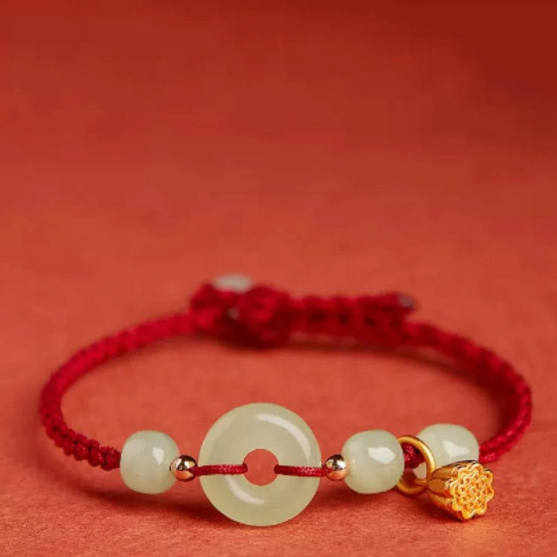 Close-up of gold lotus charm and smooth jade beads on red string