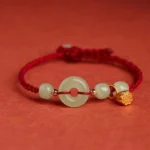 Red string jade lotus peace buckle bracelet with gold charm on warm background