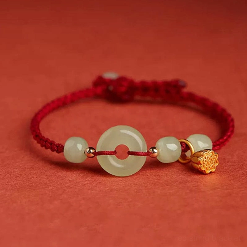 Red string jade lotus peace buckle bracelet with gold charm on warm background