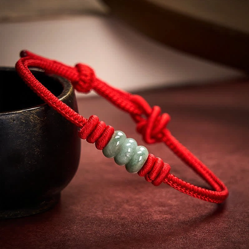 Red string jade bracelet detail showing braided cord texture and green jade beads with sliding knot