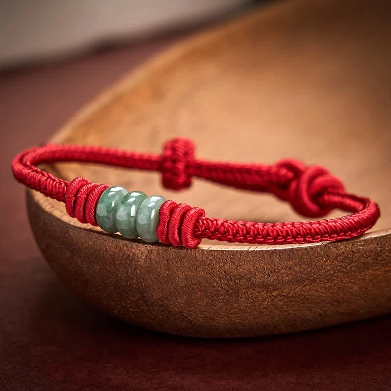 Red braided cord jade bead bracelet with adjustable knot on wooden surface