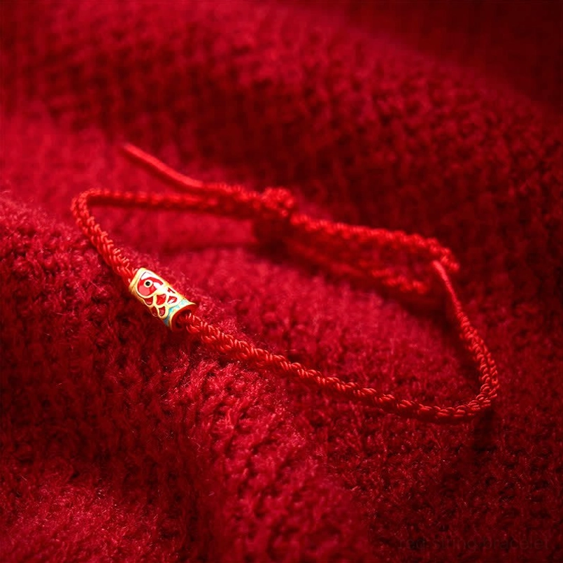 Adjustable red cord luck bracelet with koi fish pendant on knitted fabric background