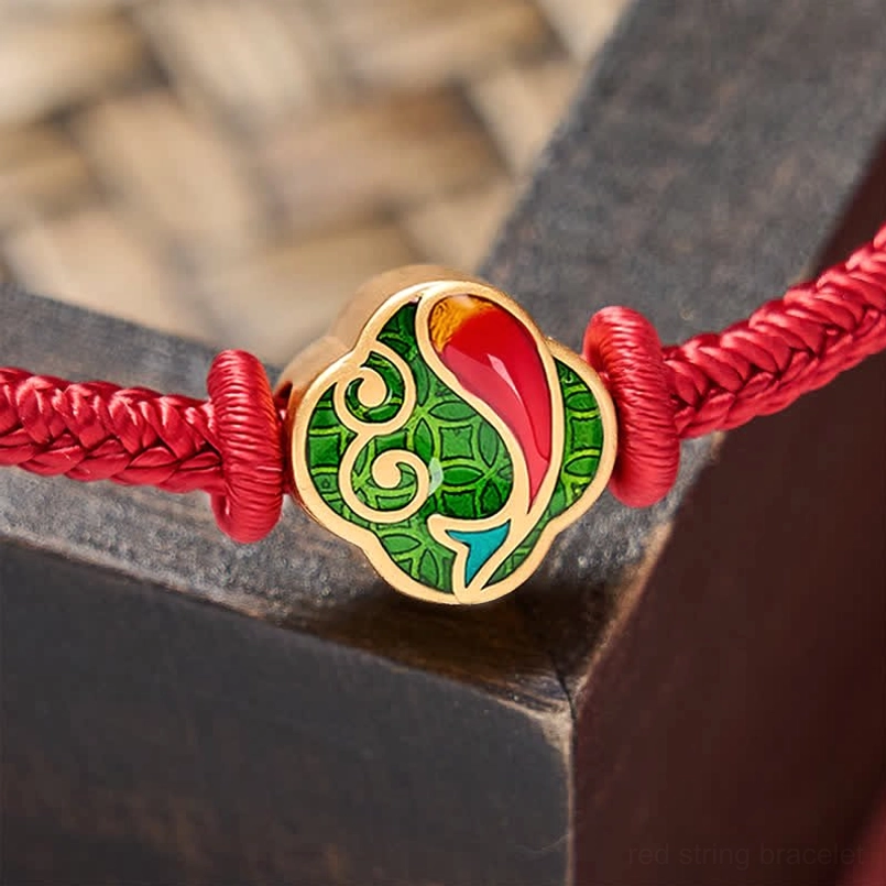 Close-up of enamel koi fish charm with gold frame on red braided cord, intricate detailing