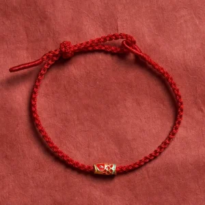 Hand-woven red string koi fish luck bracelet flat lay with enamel charm on red fabric