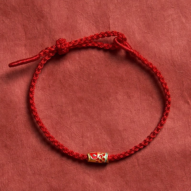 Hand-woven red string koi fish luck bracelet flat lay with enamel charm on red fabric