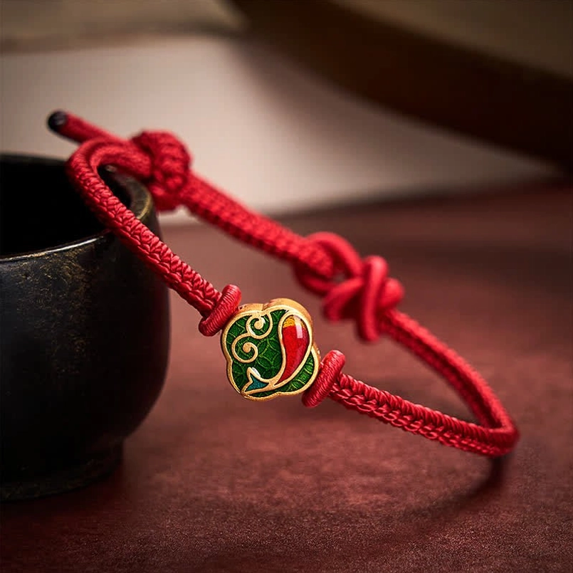 Red string bracelet with koi fish charm on wooden surface, woven cord detail close-up