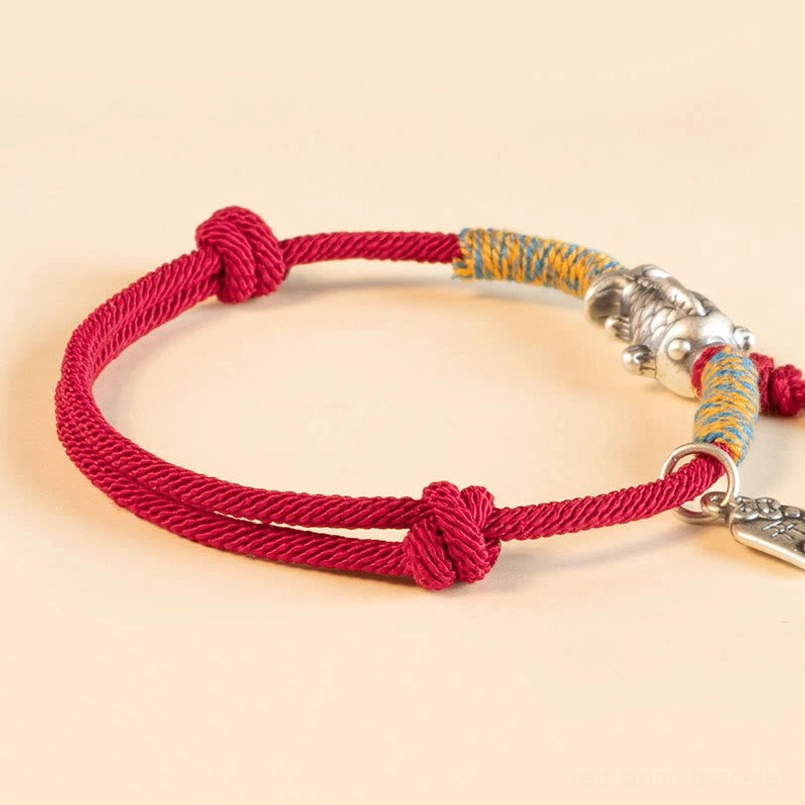 Red woven string koi bracelet with engraved silver fish charm flat lay