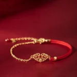 Red string lock bracelet with hollow gold-plated charm and red agate bead on dark burgundy background - front view