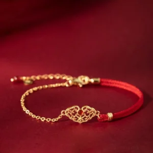 Red string lock bracelet with hollow gold-plated charm and red agate bead on dark burgundy background - front view
