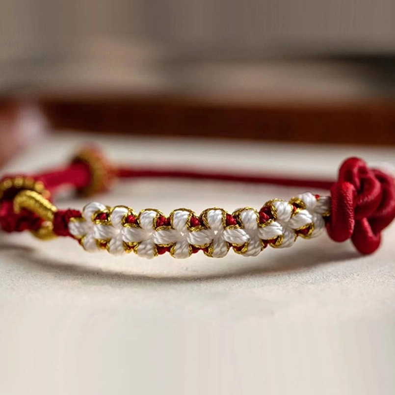 Red string bracelet low angle shot showing white-gold beaded chain and love knot centerpiece