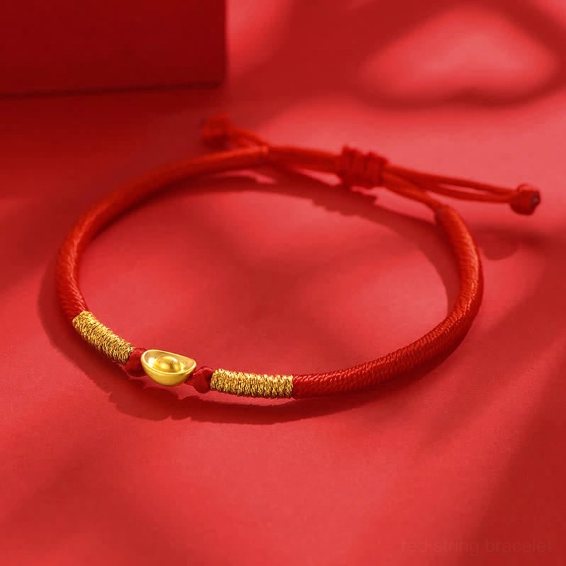 Close-up three-quarter view of red cord luck bracelet with gold twisted accents and ingot pendant