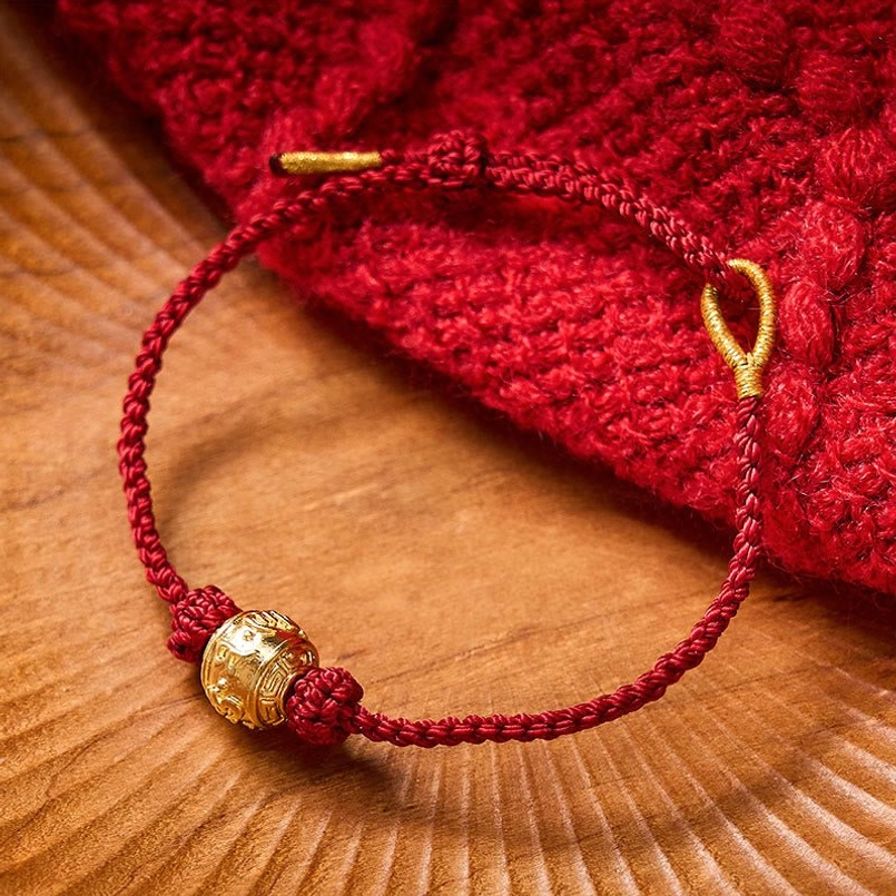 Red braided lucky bracelet with carved gold charm bead and gold loop closure on wooden background
