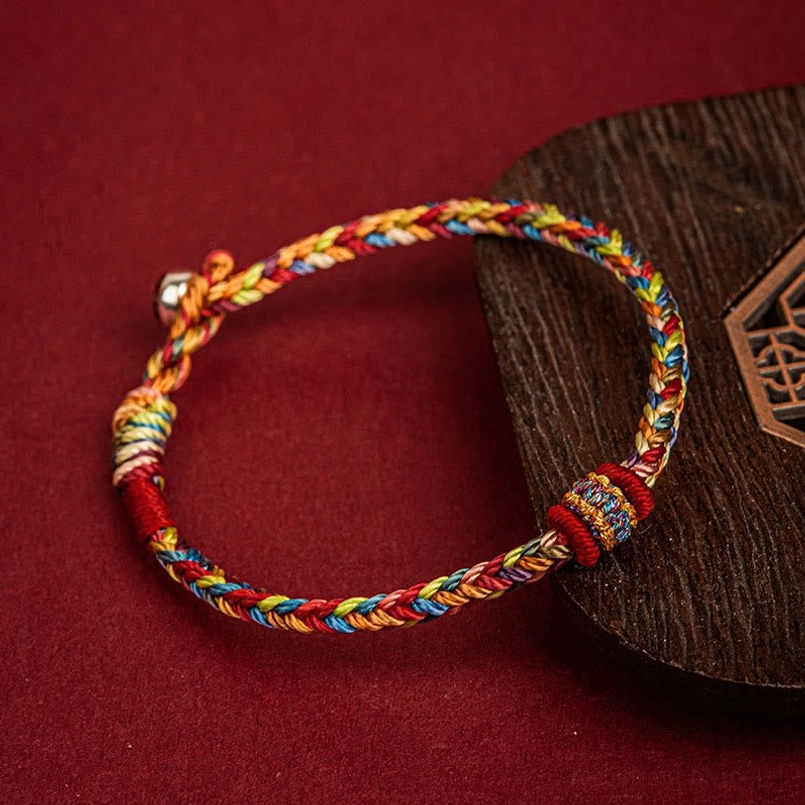 Colorful woven lucky bracelet with embroidered knot detail displayed on wooden coaster against wine red background