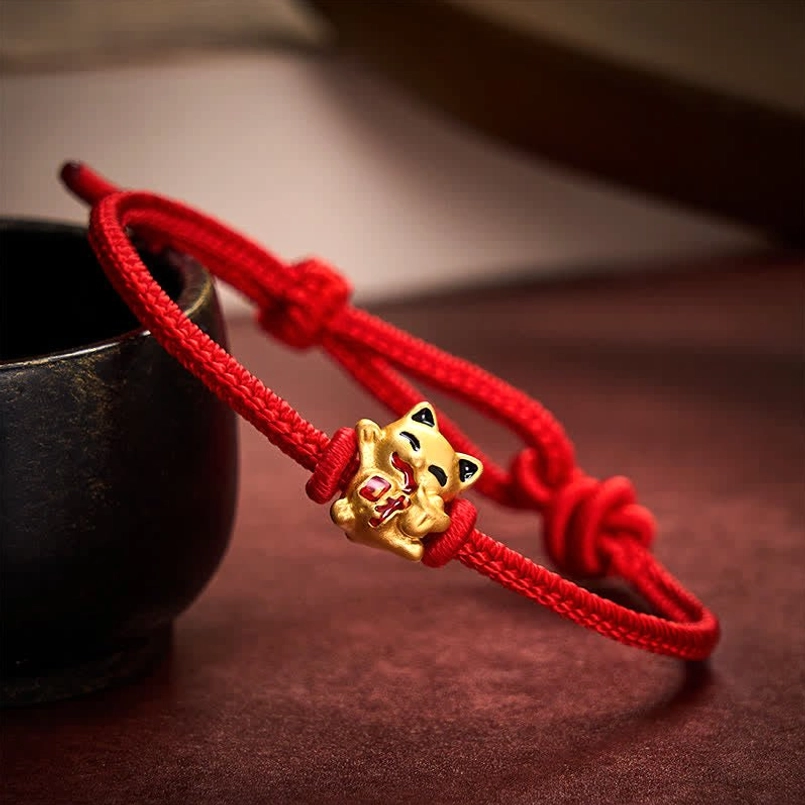 Adjustable red string lucky cat bracelet with double knots on dark brown background