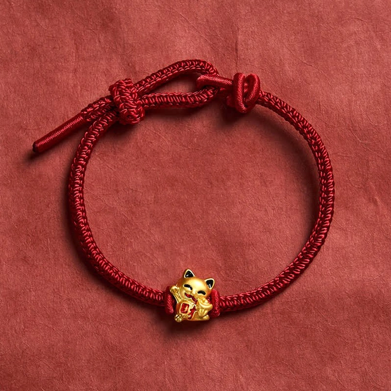 Fine braided red cord lucky cat bracelet with red accent details on dark red fabric