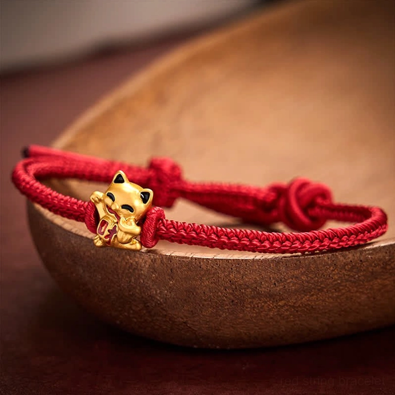 Matte golden lucky cat on red rope bracelet with dual adjustable knot structure on wooden background