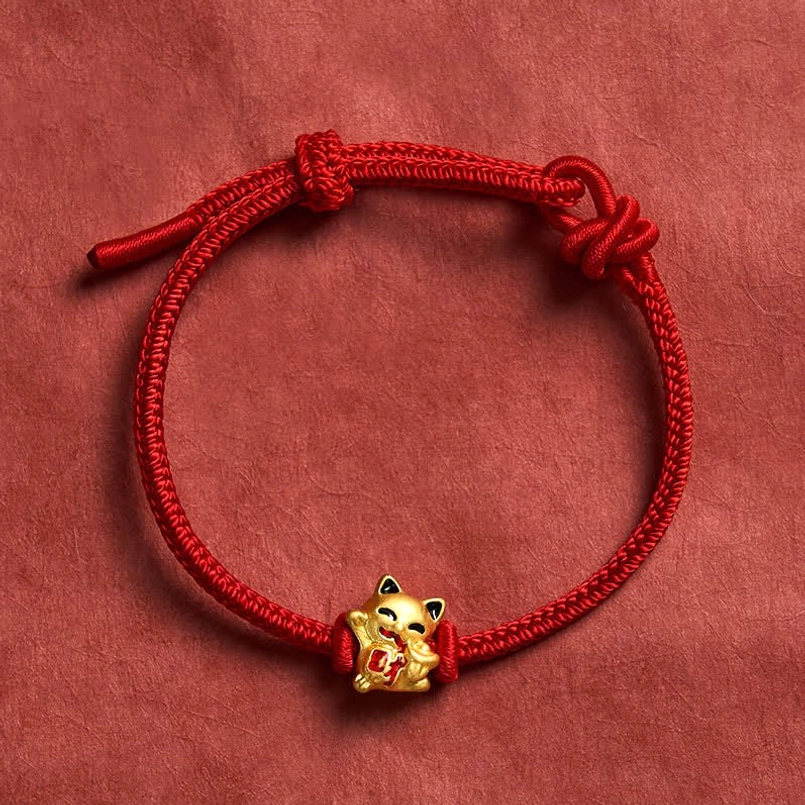 Red string lucky cat bracelet with golden charm on dark red fabric background - adjustable fortune bracelet