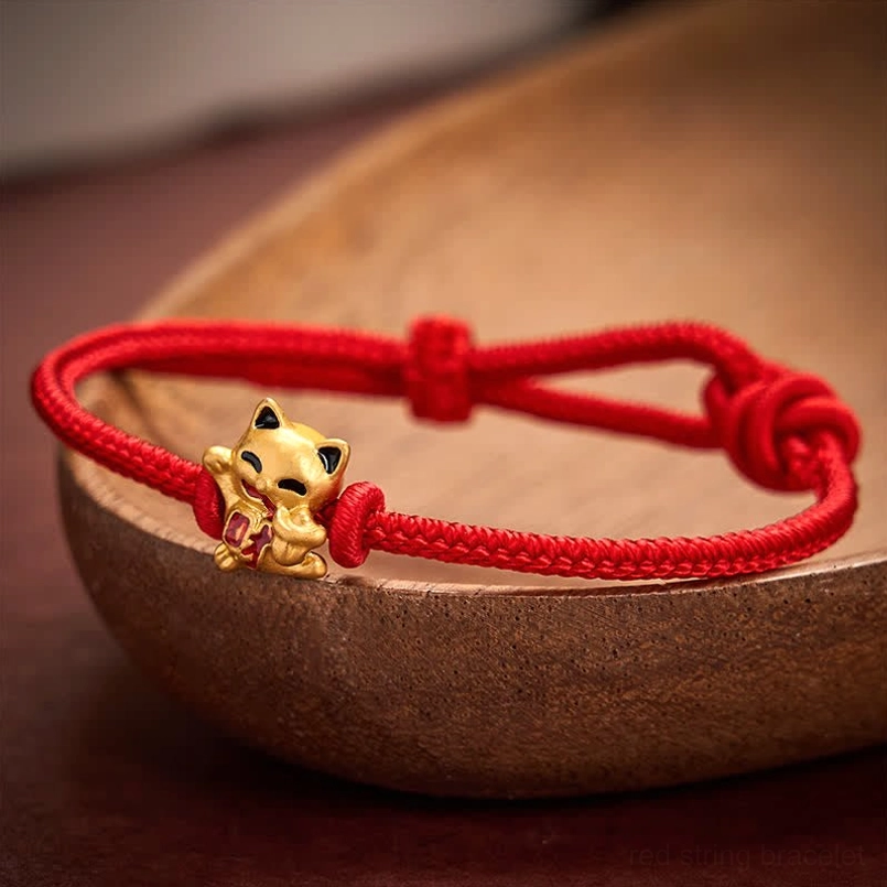 Golden lucky cat charm on red braided cord bracelet displayed on wooden tray background