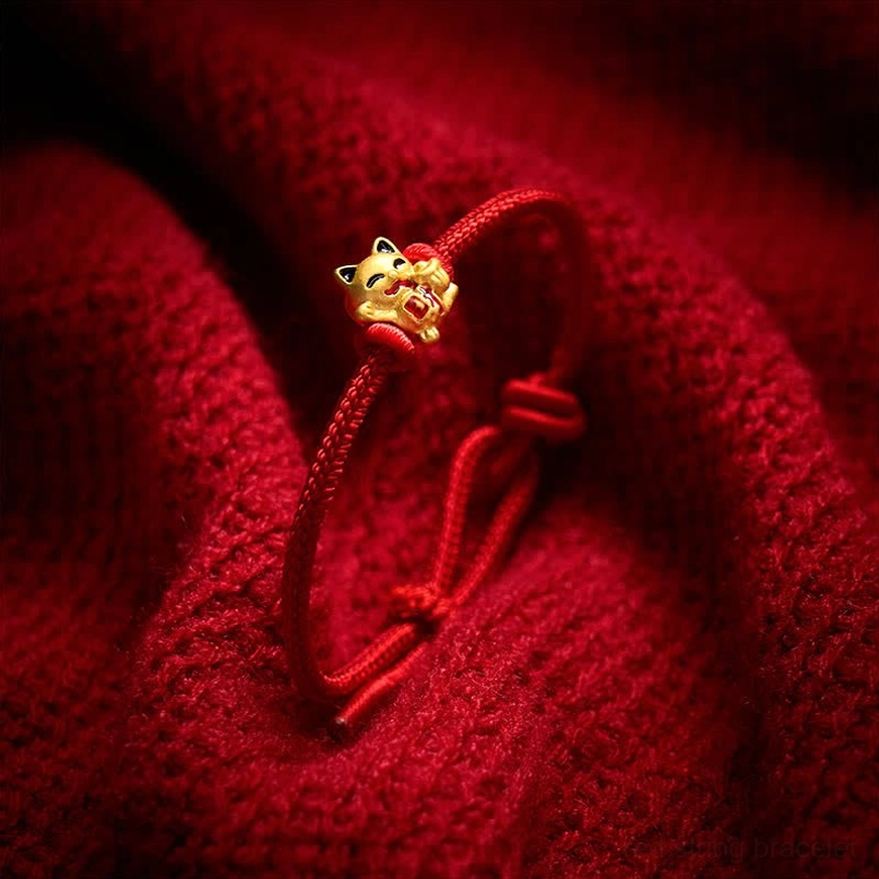 Delicate red cord bracelet with small lucky cat charm on red knitted fabric background