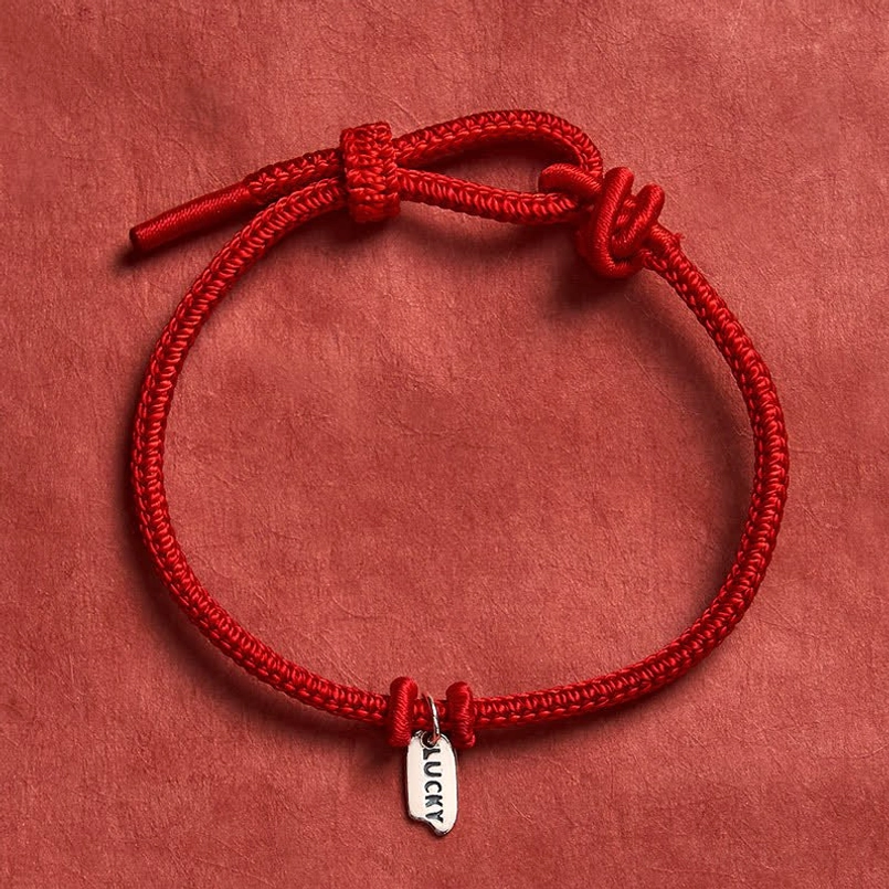 Red lucky charm bracelet with LUCKY metal tag - handmade braided cord on dark background