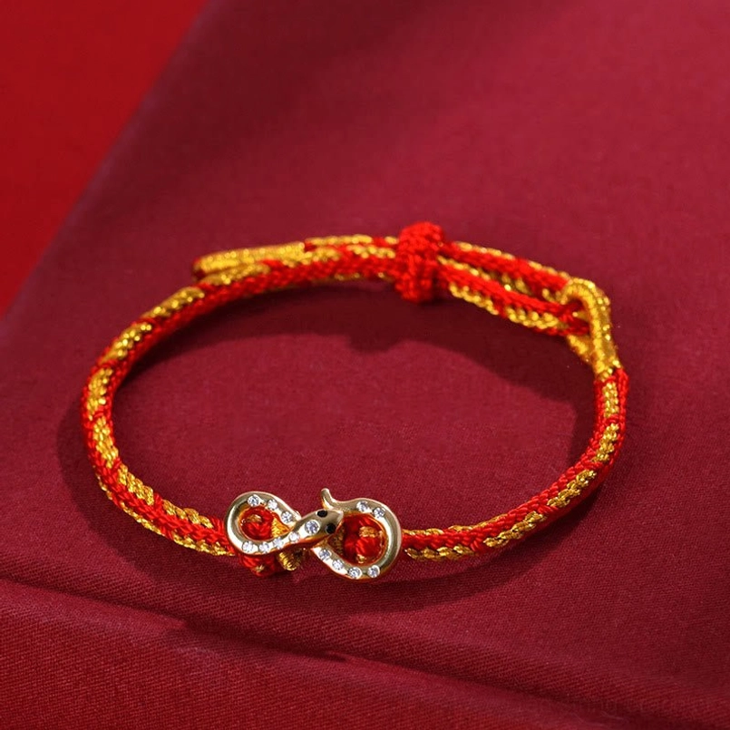 Red String Mobius Snake Bracelet with gold-tone infinity pendant and rhinestone details on red fabric background